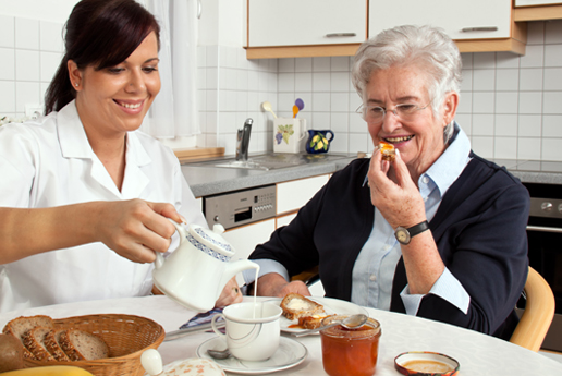 a care worker, who is providing companionship to an older person, pouring milk into a cup of tea.