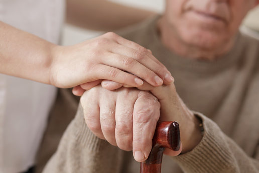 A close-up of a care worker's hand holding an older man's hand